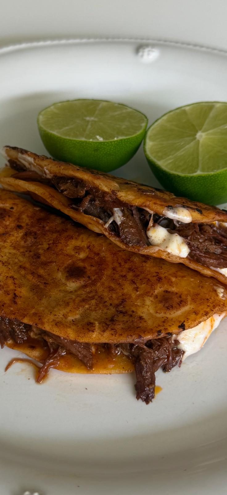 Quesabirria tacos with melted cheese and braised beef, served with lime.