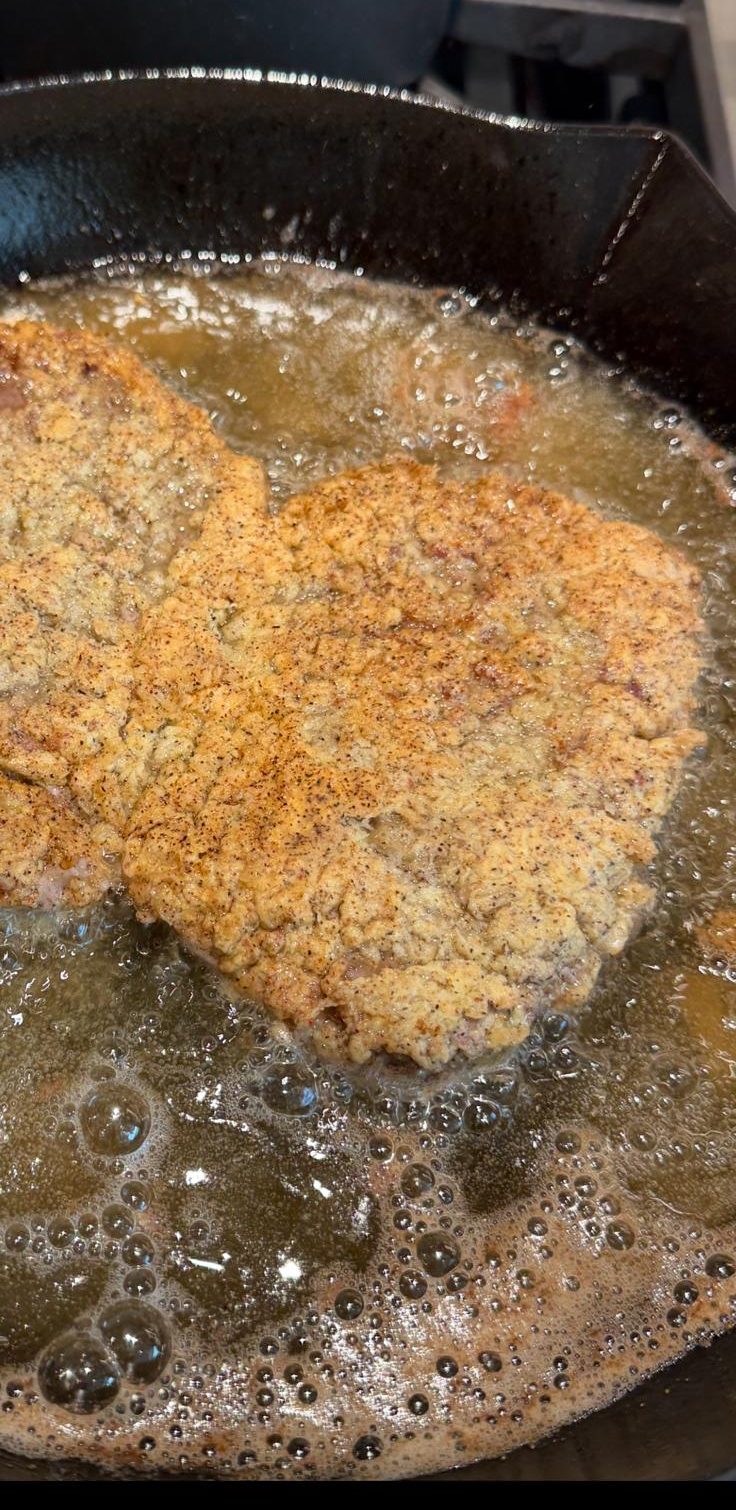 Breaded chicken shallow-frying in clear golden fat in a cast iron skillet.