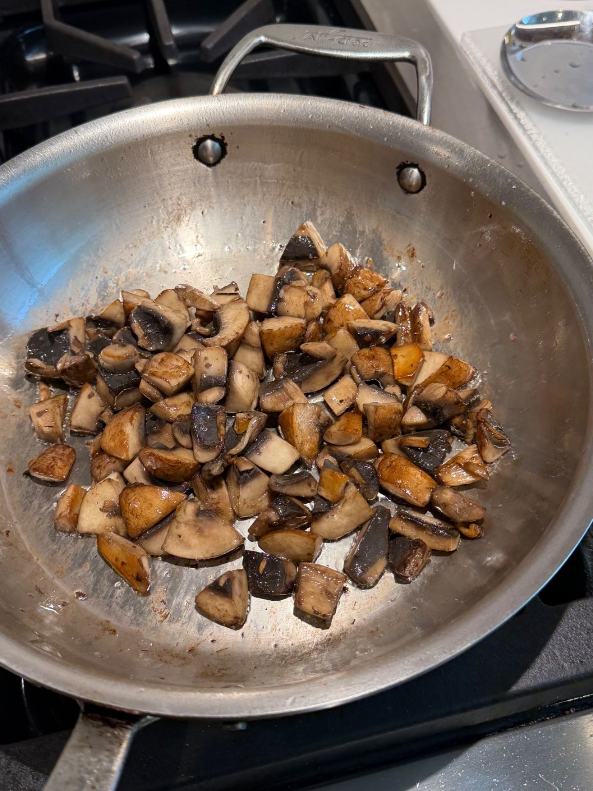 Browned mushrooms in a stainless pan with fond forming on the metal.