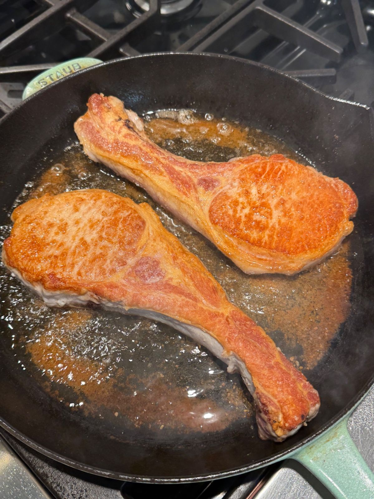 Bone-in pork chops with a deep golden crust, searing in cast iron.