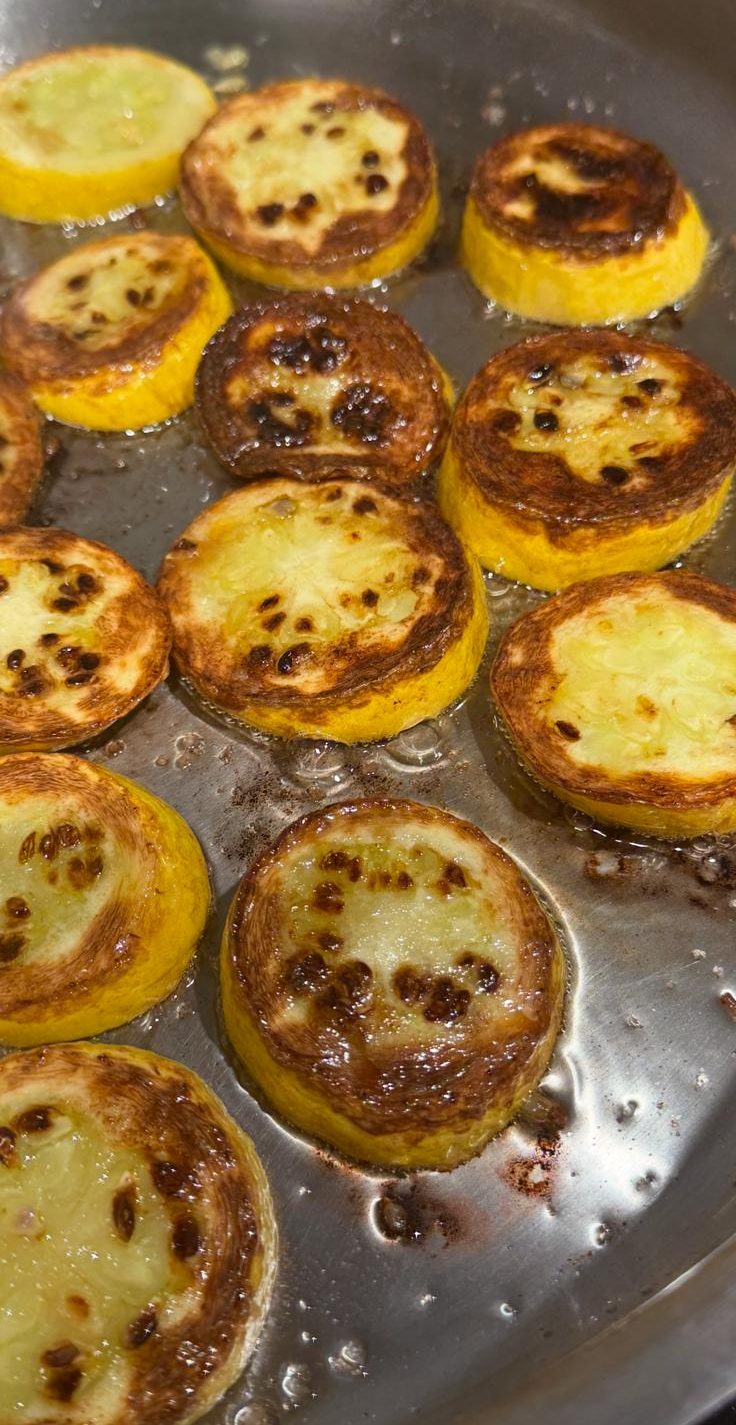 Yellow squash rounds browning in a stainless pan, deep caramelized faces, the fat still clear.